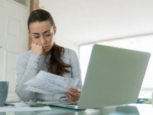 Woman reviewing high energy bills while sitting at a desk with a laptop, reflecting concerns about air conditioning efficiency and potential replacement needs.