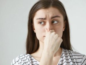 Woman pinching her nose, expressing discomfort from bad smells, related to air conditioning issues and odors in HVAC maintenance.