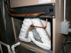 Frozen evaporator coils in an air conditioning unit, showing copper tubing and insulation, illustrating a common issue related to refrigerant leaks and HVAC system malfunctions.