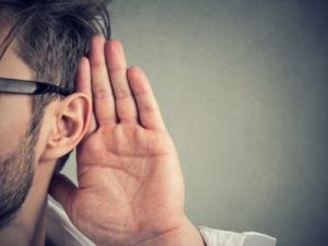 Person listening intently with hand cupped behind ear, illustrating the importance of noticing unusual sounds from air conditioning systems.