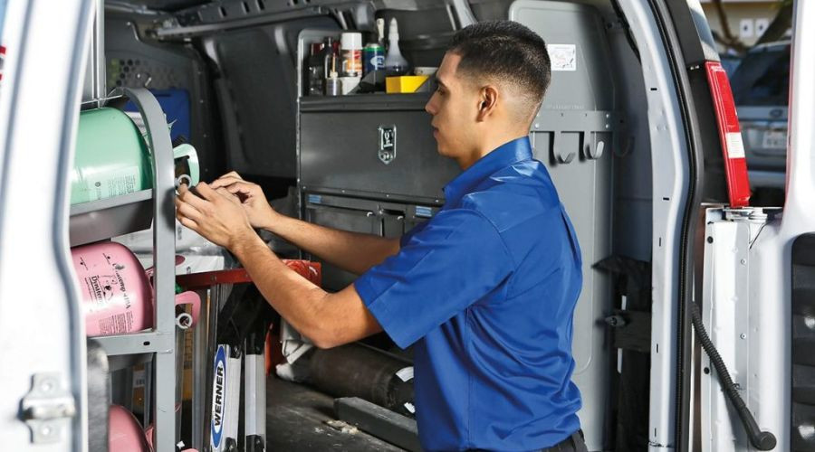 Service technician in blue uniform organizing HVAC tools and color-coded refrigerant tanks inside Air Works service van.