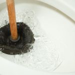 Plunger in toilet with splashing water, highlighting plumbing issues before HVAC maintenance by Air Works Heating & Air.