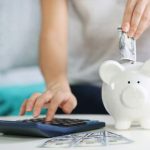 Hand placing cash into a white piggy bank, highlighting savings strategies for HVAC services by Air Works Heating & Air.