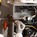 Technician repairing HVAC machinery with wrench and electrical wires, emphasizing skilled labor in maintenance.