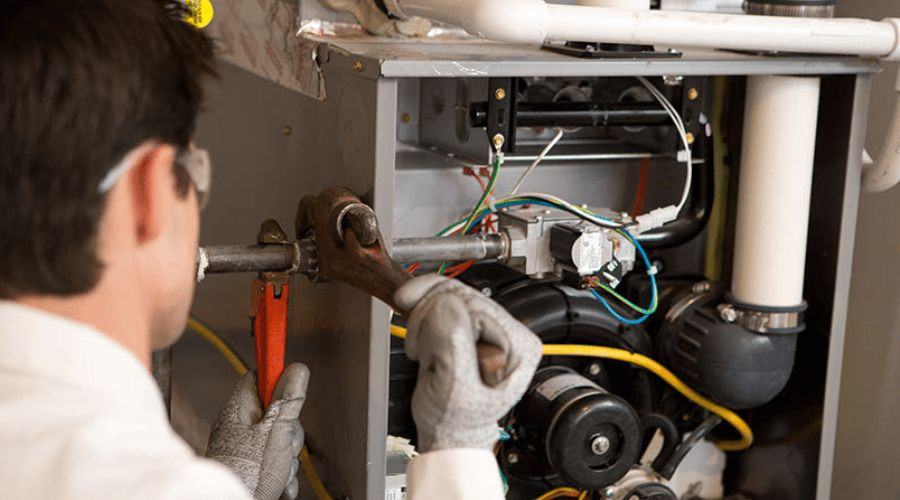 Technician repairing HVAC machinery with tools, gloves, and colorful wiring in an industrial setting.