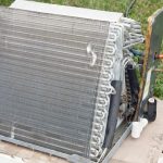 Air conditioning unit with metal coils in grassy area, near cups indicating HVAC maintenance by Air Works Heating & Air.