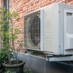 Air conditioning unit on a brick wall with a potted plant, showcasing Air Works Heating & Air in Wake Forest, NC.