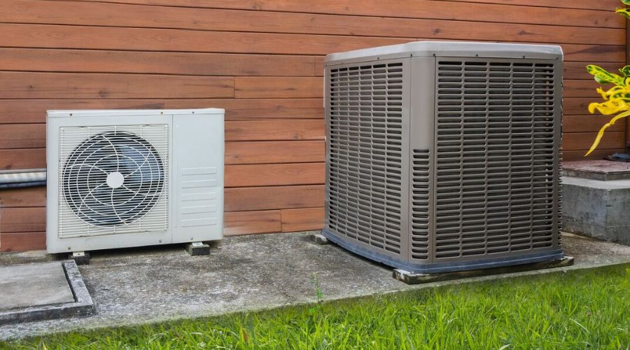 Air conditioning units on a wooden wall with grass, showcasing Air Works Heating & Air's HVAC solutions in Wake Forest, NC.