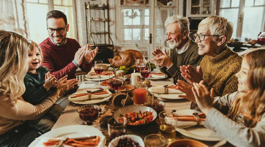 Diverse group enjoying a festive dinner with turkey, salads, and beverages at a table, showcasing family togetherness.