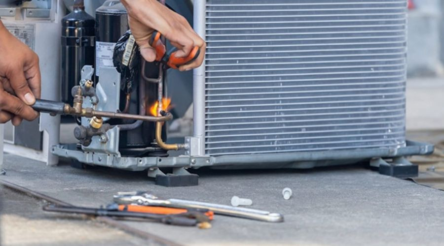 Technician servicing an AC unit with a wrench and torch, flames visible from the pipe, showcasing HVAC repair by Air Works.