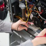 Technician's hands using a multimeter on colorful electrical components during HVAC repair at Air Works Heating & Air.