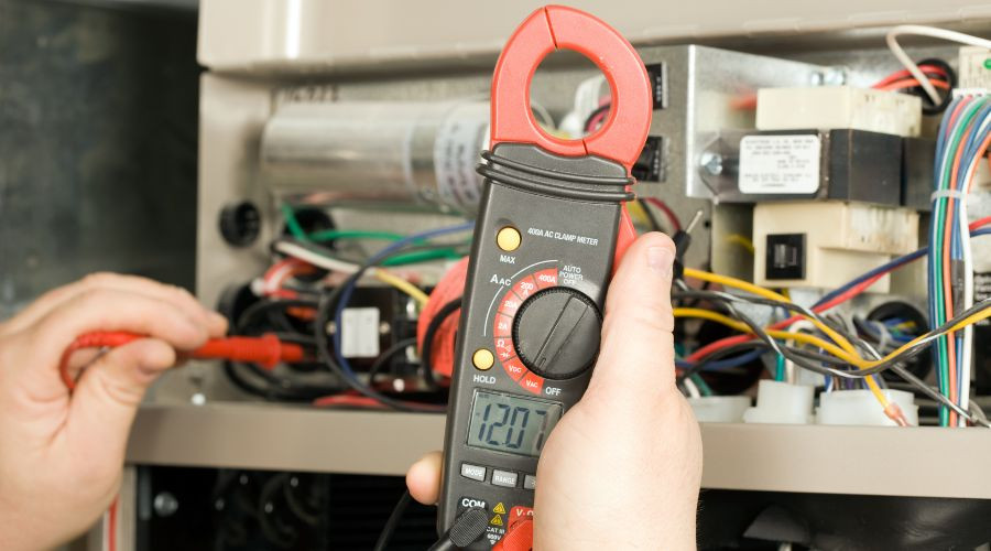 Technician using a digital clamp meter to check electrical wiring for HVAC maintenance at Air Works Heating & Air.