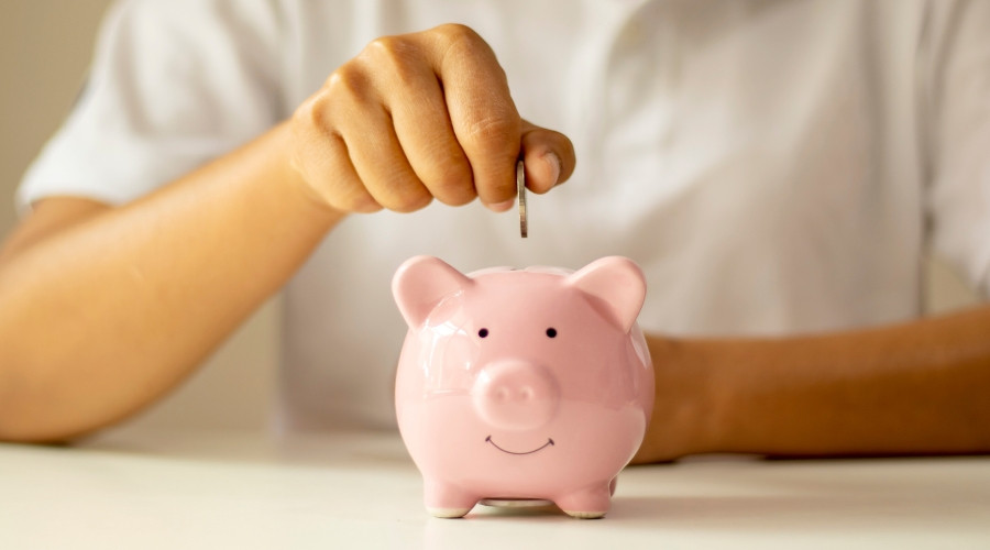 Person inserting a coin into a pink piggy bank, symbolizing savings and cost reduction related to HVAC services and energy efficiency.